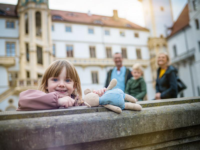 5jähriges Mädchen steht an einem Brunnen und lächelt, dahinter ragt der Große Wendelstein empor.