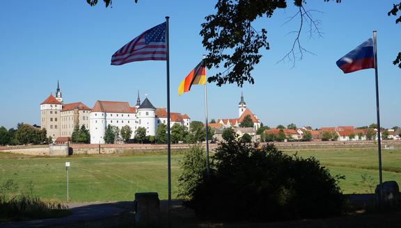 Blick über die Elbwiesen auf das Schloss, im Vordergrund Flaggen der Länder USA, Deutschland und Russland, die im Wind flattern