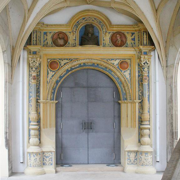 Blick auf das Portal. Oberhalb der Tür thront eine Büste Friedrich des Weisen, rechts und links davon sind Medaillons von Kurfürst Johann Friedrich und seiner Frau Sybille angebracht. Rechts und links von der Tür strecken sich zwei Säulen empor, an denen kleinere Medaillons von Martin Luther und Philipp Melanchton befestigt sind.